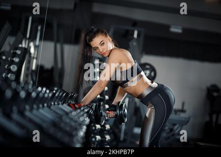 Mince, bodybuilder fille, soulève lourd haltère debout devant le miroir pendant l'entraînement dans la salle de gym. Concept sportif, combustion de graisse et une vie saine Banque D'Images