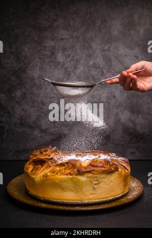 Tarte aux pommes. Sucre en poudre. Arrière-plan sombre. La tarte aux pommes juste en dehors du four est arrosée de poudre de sucre Banque D'Images