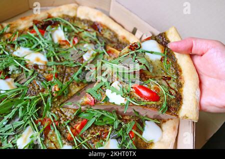 Cueillir à la main une tranche de pizza Arugula Balsamic dans une boîte en papier Banque D'Images