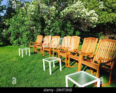 Les confortables chaises en bois et les petites tables dans un jardin ensoleillé avec de l'herbe verte et des arbres en fleurs Banque D'Images