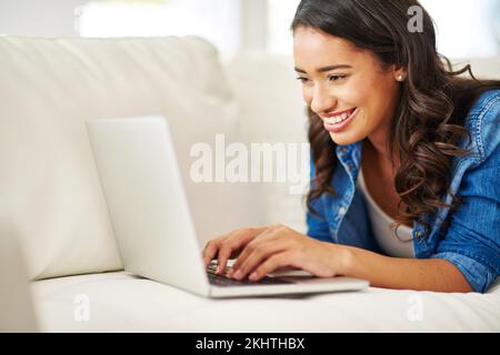 Ordinateur portable, femme noire posée sur un canapé pour écrire des e-mails, consulter des réseaux sociaux ou regarder des films en streaming à la maison. Week-end, femme sur un canapé avec ordinateur et se détendre Banque D'Images