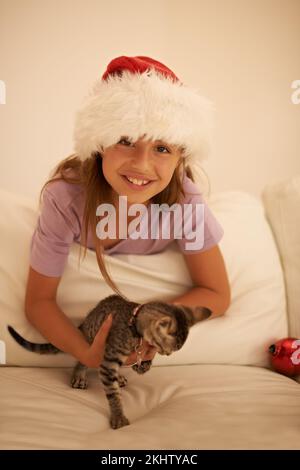 Fille, fête de Noël et cadeau chaton dans la chambre à coucher pour célébrer des vacances festives. Enfant heureux, chat d'animal de compagnie comme cadeau de fête et de soin des animaux ou des enfants