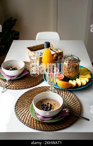 Petit déjeuner frais nourrissant avec porridge, fruits et jus d'orange sur une table intérieure. Repas copieux avec flocons d'avoine et fruits de saison sur un tableau blanc Banque D'Images