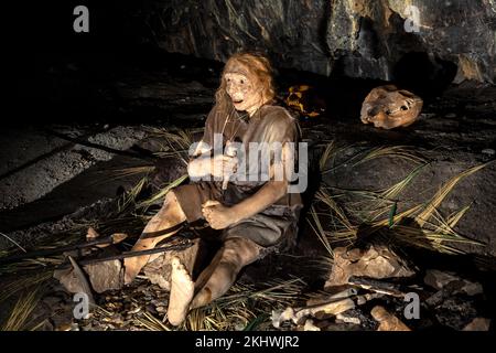 Reconstruction d'une scène paléolithique du milieu dans la Grotta Nera. Tribu primale des anciens sauvages peau d'animal et des axes de pierre mangeant la viande friture sur Banque D'Images