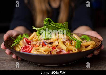 Femme non reconnaissable, écourtée en tenue noire tenant juteux, prêt à manger, macaroni bio frais avec jambon, légumes Banque D'Images