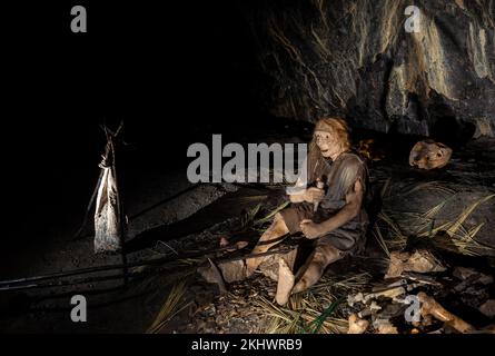 Reconstruction d'une scène paléolithique du milieu dans la Grotta Nera. Tribu primale des anciens sauvages peau d'animal et des axes de pierre mangeant la viande friture sur Banque D'Images