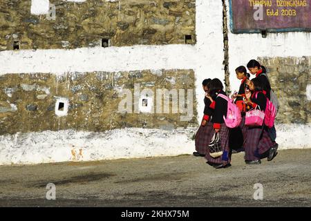 Des écoliers bhoutanais en uniforme se promènent le long d'une route après avoir descendre du bus scolaire dans un après-midi ensoleillé à Thimphu Bhoutan. Banque D'Images