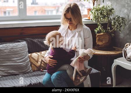 Vue latérale de la petite fille blonde s'asseoir sur le médecin des enfants, regardant le pédiatre visite patient à la maison. Visite d'infirmière. Banque D'Images