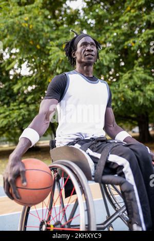 Joueur professionnel de basket-ball sur chaise roulante, athlète africain avec handicap jouant le panier sur le sol avec détermination et force de volonté Banque D'Images