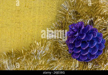 Décoration de Noël avec un cône de pin violet et une guirlande dorée brillante sur un fond doré avec texture. Banque D'Images