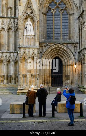 Personne prenant des photos de la nouvelle statue Elizabeth 2 sur une niche portant des robes de chambre (orbe, armusier) - York Minster West front, North Yorkshire, Angleterre, Royaume-Uni. Banque D'Images