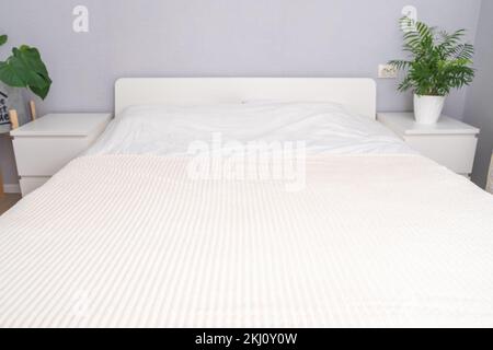 Une belle chambre blanche moderne avec un grand lit spacieux, avec des draps blancs frais, meublé de plantes vertes. Belle chambre d'hôtel avec un grand lit linge blanc, avec des plantes vertes sur les tables de chevet. Banque D'Images