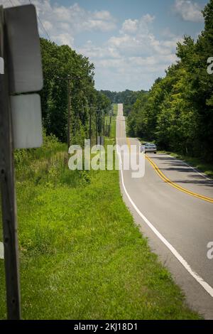 Long chemin d'asphalte droit avec des lignes jaunes et blanches en Amérique, traverse une petite vallée entourée d'arbres et d'herbe Banque D'Images