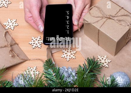 Objectifs plans faire à faire et liste de souhaits pour le nouveau concept de Noël année. Mains de femme tenant le téléphone mobile sur fond de bois avec des cadeaux de Noël, Fir Banque D'Images