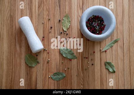 Un mortier en pierre pour épices est posé sur une table en bois. Sur la table se trouvent des feuilles de lavande et un mélange de grains de poivre. Banque D'Images