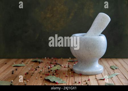 Un mortier en pierre pour épices est posé sur une table en bois sur fond noir. Sur la table se trouvent des feuilles de lavande et un mélange de grains de poivre. Banque D'Images