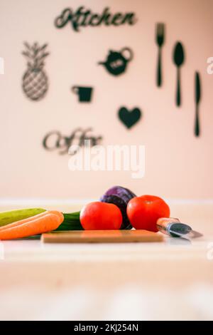 Vue latérale d'un couteau et d'une planche à découper en bois entourés d'un assortiment de légumes crus sur le comptoir de cuisine. Mise au point sélective. Banque D'Images