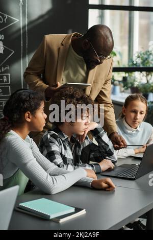 Professeur afro-américain montrant le travail de programme d'ordinateur sur ordinateur portable aux enfants pendant la leçon DE TI Banque D'Images