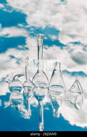 Divers verres de laboratoire sur fond miroir avec reflet du ciel. Essais conceptuels en laboratoire et recherche sur les phénomènes et les ressources naturelles Banque D'Images