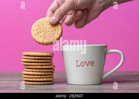 Main prenant un biscuit à côté d'une tasse avec « Love » écrit dessus. Concept thé et biscuit. Banque D'Images