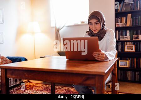 Jolie jeune femme du Moyen-Orient portant le hijab à l'aide d'un ordinateur portable à la maison. Une jeune fille musulmane se prépare aux examens d'entrée. Éducation à domicile et concept de studing en ligne Banque D'Images