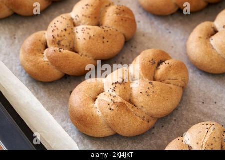 Petits pains tressés ou petits pains faits de farine d'épeautre de grain entier, saupoudrée de graines de pavot, sur une plaque à pâtisserie Banque D'Images