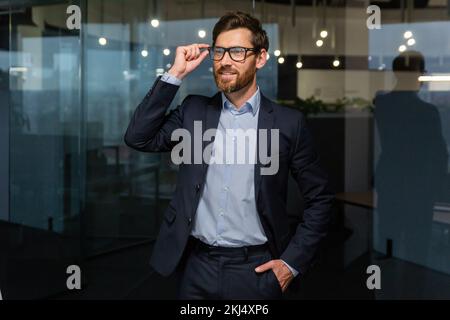 Portrait d'un homme d'affaires prospère patron mûr en costume d'affaires, homme travaillant à l'intérieur du bureau au travail en lunettes regardant loin, investisseur senior avec la barbe souriante et rêveuse. Banque D'Images