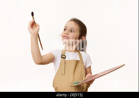 Portrait sur fond blanc de l'enfant d'âge préscolaire, petite fille mignon tient une palette de peintures, peinture avec un pinceau Banque D'Images
