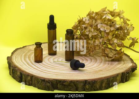 Maquette de flacons en verre brun avec couvercle compte-gouttes sur panneau en bois. Flacons en verre vides avec pipette, fleur d'hortensia séchée sur fond jaune. Concept o Banque D'Images