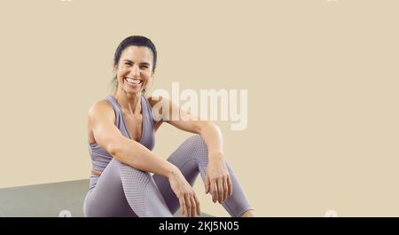 Joyeuse femme de sport qui est prête pour l'entraînement sportif se trouve sur un tapis de sport sur fond beige. Banque D'Images