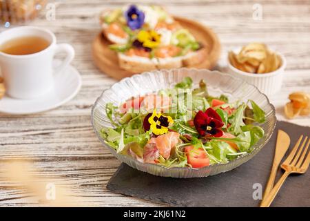 Salade méditerranéenne pescétarienne saine avec saumon fumé, légumes, légumes verts et fleurs comestibles. Thé avec hors-d'œuvre. Dîner sain Banque D'Images