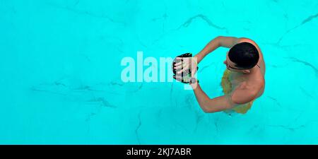 Des trains d'homme dans la piscine. Vue d'en haut sur un nageur ailetique homme nageant dans l'eau claire bleue portant des lunettes pour nager et utiliser des palettes à main Banque D'Images