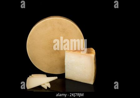 Un fromage avec une texture à son arrière isolé sur un fond noir à côté d'un coin et des tranches de fromage. Banque D'Images