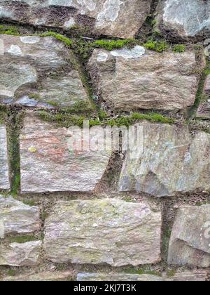 Un plan vertical de mur d'un bâtiment fait de vieilles pierres de granit avec de la mousse verte entre les deux Banque D'Images