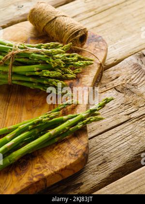 Beaucoup d'asperges fraîches sur une planche à découper. À proximité se trouve une pelote de ficelle sur une simple table en bois. Cuisiner des plats sains avec des asperges. Recettes, coo Banque D'Images