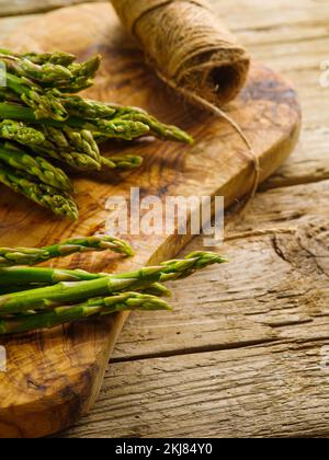 Beaucoup d'asperges fraîches sur une planche à découper. À proximité se trouve une pelote de ficelle sur une simple table en bois. Cuisiner des plats sains avec des asperges. Recettes, coo Banque D'Images