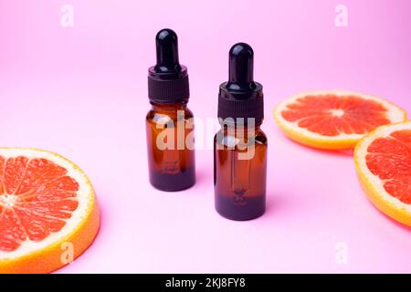 Huile essentielle de pamplemousse dans des flacons compte-gouttes bruns en verre sur fond rose avec fruits frais, cosmétiques et spa Banque D'Images