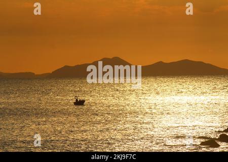 Coucher de soleil en mer, avec la silhouette d'un petit bateau flottant dans les reflets du soleil, avec les montagnes Cantabriques en arrière-plan, vu de Gorliz Banque D'Images