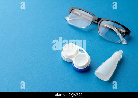 Composition de lunettes avec boîtier pour lentilles de contact et gouttes pour les yeux et sur fond bleu avec espace de copie Banque D'Images