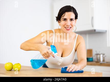 Jeune femme hispanique souriante essuyant les surfaces de la cuisine à la maison Banque D'Images