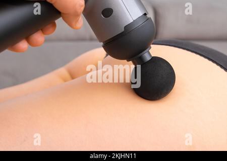 Homme massant la jambe de l'utérus à l'aide d'un pistolet de massage. Physiothérapie ou thérapie par percussion Banque D'Images