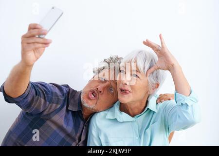 L'amour est de trouver quelqu'un pour être étrange avec. un couple affectueux qui joue tout en prenant des photos d'eux-mêmes avec un téléphone portable. Banque D'Images