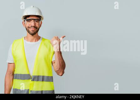 Portrait d'un ingénieur pointant de côté. Travailleur de la construction avec gilet pointant vers une publicité. Ingénieur homme pointant vers le côté. Ingénieur concepteur p Banque D'Images