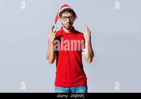 Beau homme en chapeau de noël faisant un souhait sur fond isolé. Guy avec chapeau de noël faisant un souhait sur fond isolé, homme plein d'espoir dans le christ Banque D'Images