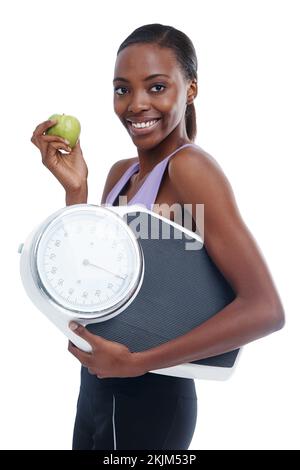 Enfin à mon objectif de poids. Portrait isolé d'une jeune femme sportive tenant une balance et une pomme. Banque D'Images