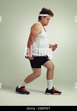 Can you see it working. Side view shot of an overweight man lifting dumbbells. Stock Photo