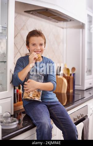 Mains dans le pot à biscuits. Un jeune garçon mangeant un cookie tout en tenant un pot à biscuits. Banque D'Images