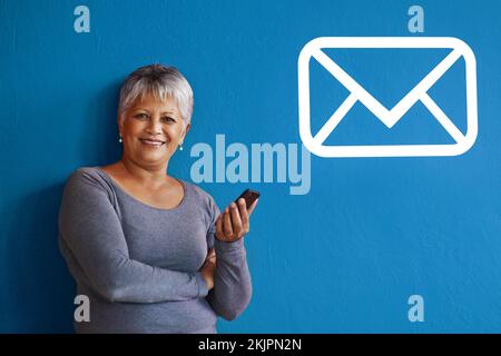 Faites passer un jour à quelqu'un, envoyez-lui un message. une femme mûre tenant un téléphone portable avec une icône de message à côté d'elle sur le mur. Banque D'Images