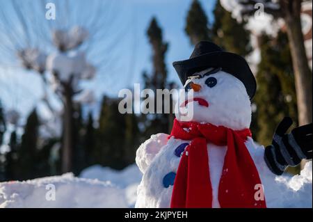 Un bonhomme de neige avec une grimace créepy dans un chapeau et un foulard. Banque D'Images