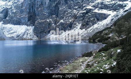 Czarny Staw Pod Rysamy ou lac Black Pond près de la cabane de montagne Morskie Oko Snowy dans les montagnes polonaises de Tatry, vue sur les drones, Zakopane, Pologne. Vue aérienne prise de magnifiques collines verdoyantes et montagnes dans des nuages sombres et reflet sur le lac Morskie Oko. Destination touristique de voyage Banque D'Images
